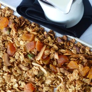 A close up of Pistachio Apricot Granola on the baking pan with a pitcher of milk beside it.