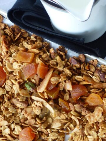 A close up of Pistachio Apricot Granola on the baking pan with a pitcher of milk beside it.