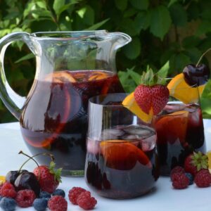 A pitcher and two glasses of Prosecco Berry Sangria surrounded by fresh fruit.