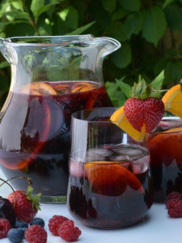 A pitcher and two glasses of Prosecco Berry Sangria surrounded by fresh fruit.