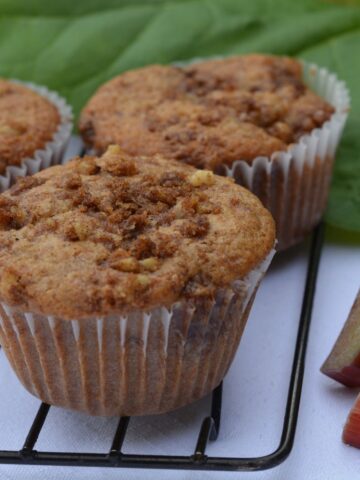 A baking rack with rhubarb streusel muffins surrounded by chopped rhubarb and a rhubarb leaf.