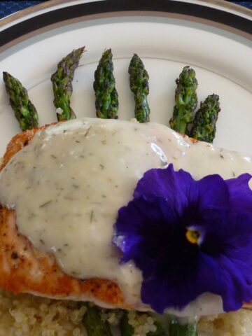 Grilled Salmon with West Coast Dill Barbecue Sauce on top of cooked asparagus with a purple pansy garnish.