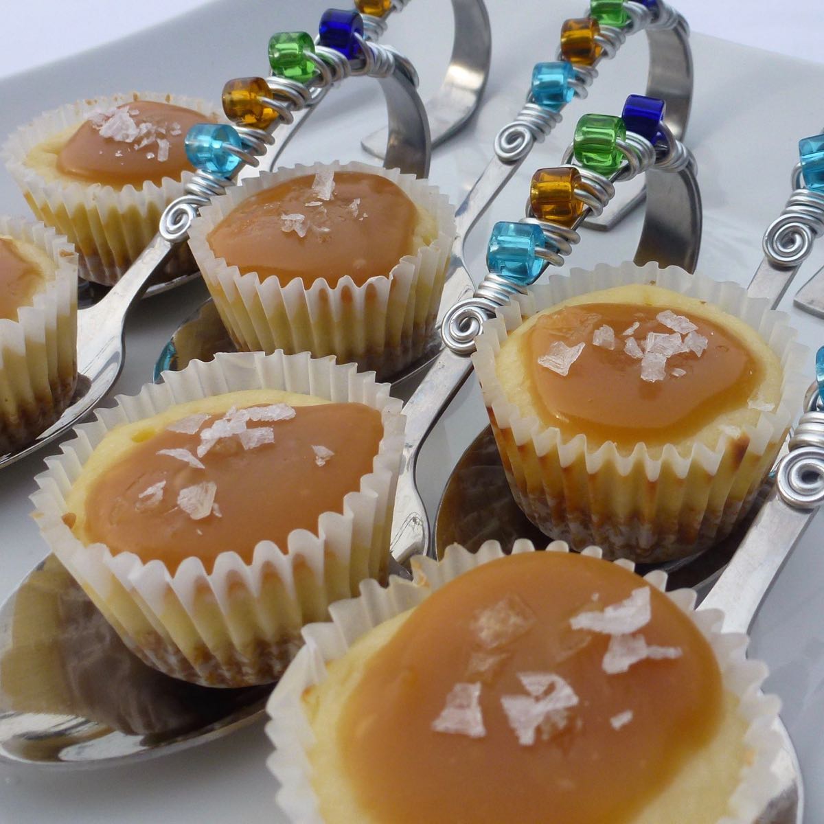Salted Caramel Cheesecake Cupcakes served on fancy spoons with colourful beaded handles.