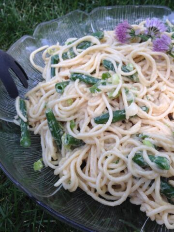 A close up of Spicy Sesame Noodle Salad with green beans and a sprinkling of fresh chives and purple chive blossoms.