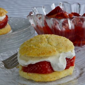 Strawberry Shortcake on a plate filled with strawberry sauce and whipped cream, with more in the background.