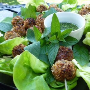 A platter of spicy Thai meatballs in lettuce cups garnished with fresh mint leaves and a dish of cilantro ponzu sauce on the side.