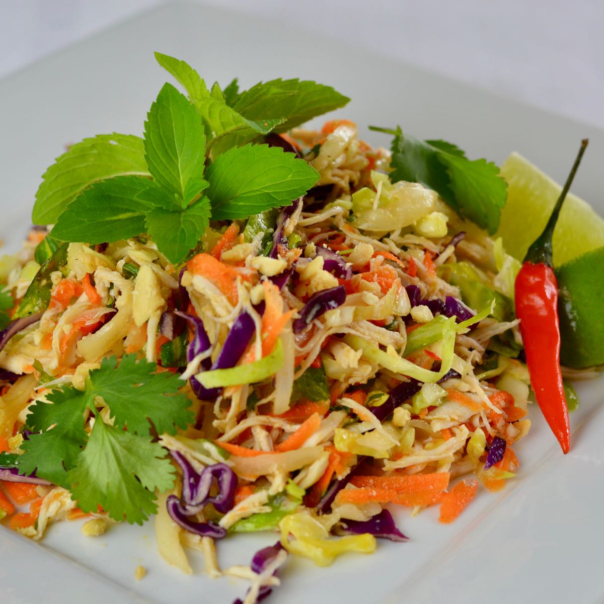 A white plate with Vietnamese Cabbage Chicken Salad garnished with peanuts, mint, cilantro and fresh lime.
