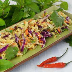 A green plate with Vietnamese Cabbage Chicken Salad garnished with peanuts, fresh mint and cilantro.