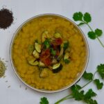 A bowl of Yellow Split Pea Dal topped with sauteed zucchini, tomato and spices.