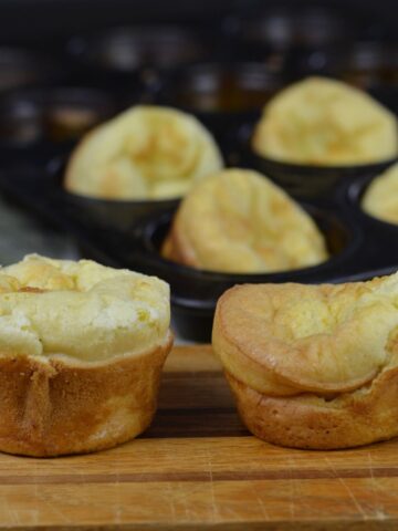 Two Gluten Free Yorkshire Puddings on a board in front of a muffin tin full of more.
