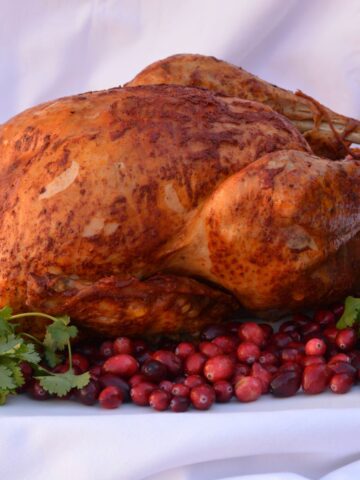 A whole Achiote Butter Basted Turkey on a platter surrounded by cranberries and cilantro.