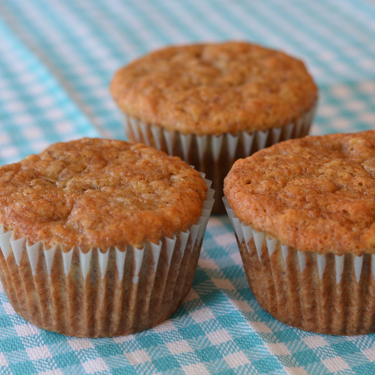 Three gluten free Banana Muffins resting on a turquoise tea towel.