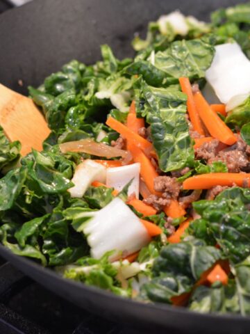 A wok full of raw bok choy and julienned carrot on top of the beef.