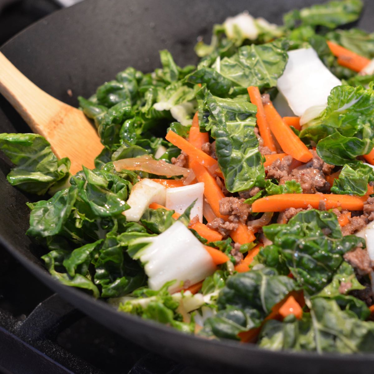 A wok full of raw bok choy and julienned carrot on top of the beef.