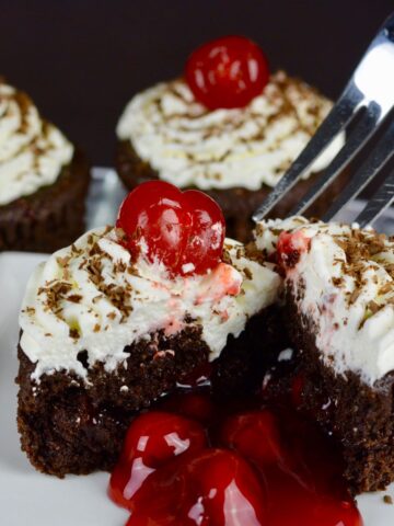 A fork digging into a gluten free Black Forest Cupcake with the cherry pie filling oozing out onto the plate.