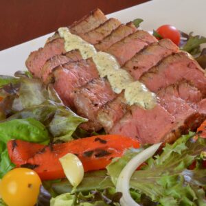 A plate of Blackened Steak Salad with peppers, tomato, onion and blue cheese dressing.