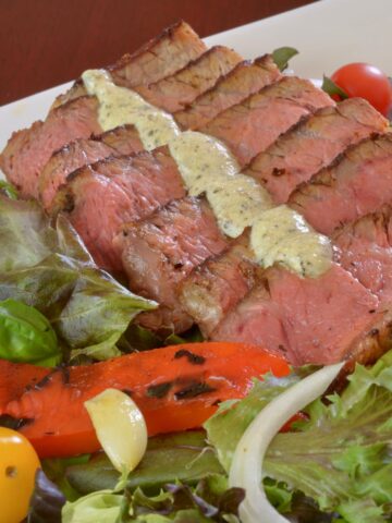 A plate of Blackened Steak Salad with peppers, tomato, onion and blue cheese dressing.
