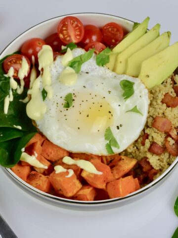A Breakfast Power Bowl filled with cooked quinoa, avocado, spinach, tomatoes and egg and topped with hollandaise sauce for a special treat.