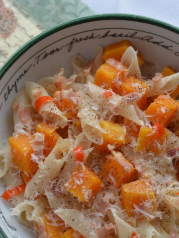 A bowl of Butternut Squash and Pancetta Penne sprinkled with freshly grated Parmesan cheese.