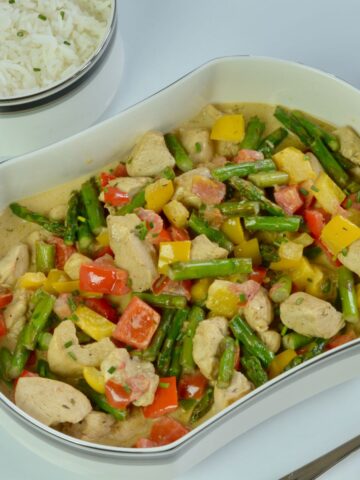 A serving dish of Chicken in Madeira Cream Sauce, asparagus, red and yellow peppers.