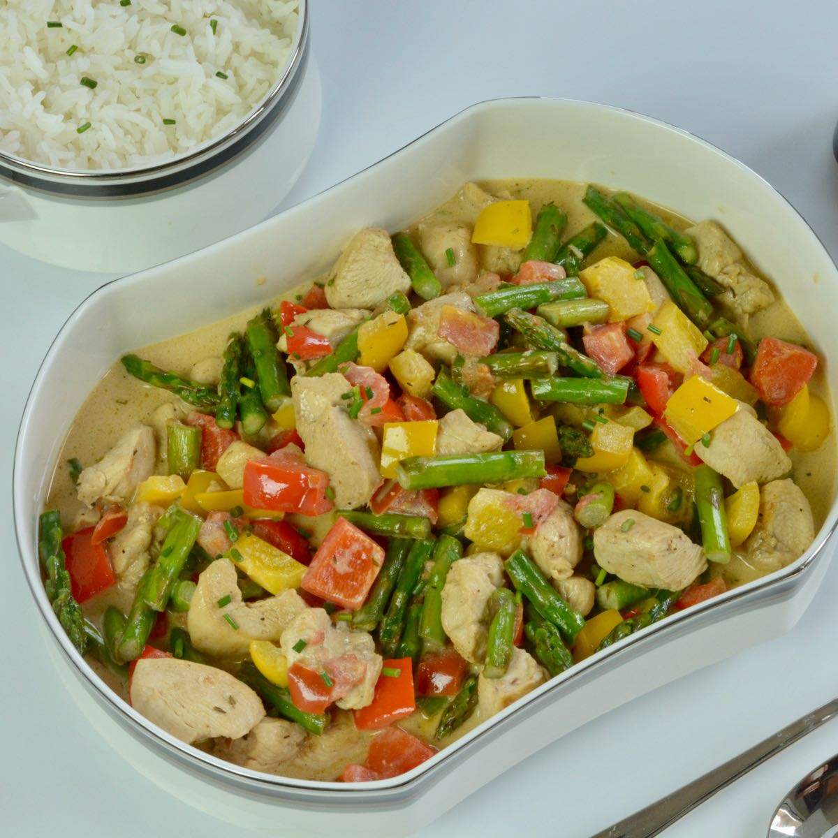A serving dish of Chicken in Madeira Cream Sauce with asparagus, red and yellow peppers plus a side dish of rice.