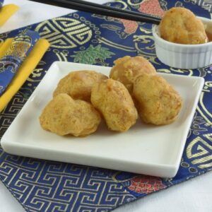 A small plate of Chinese Chicken Balls with plum sauce on top of an blue placemat with an Oriental pattern.
