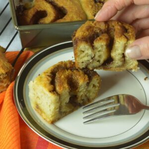 A biscuit cinnamon roll on a plate cut in half, surrounded by other cinnamon rolls in and out of the baking pan.