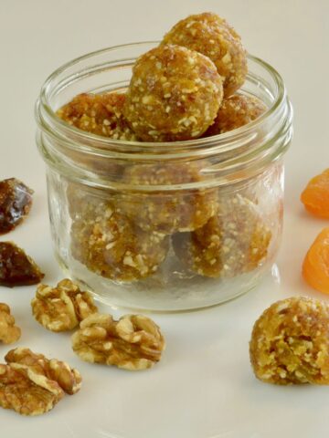 A Mason jar filled with Coconut Date Energy Balls surrounded by dates, apricots and walnuts.