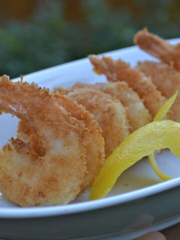 A serving dish filled with gluten free coconut shrimp garnished with a twist of lemon.