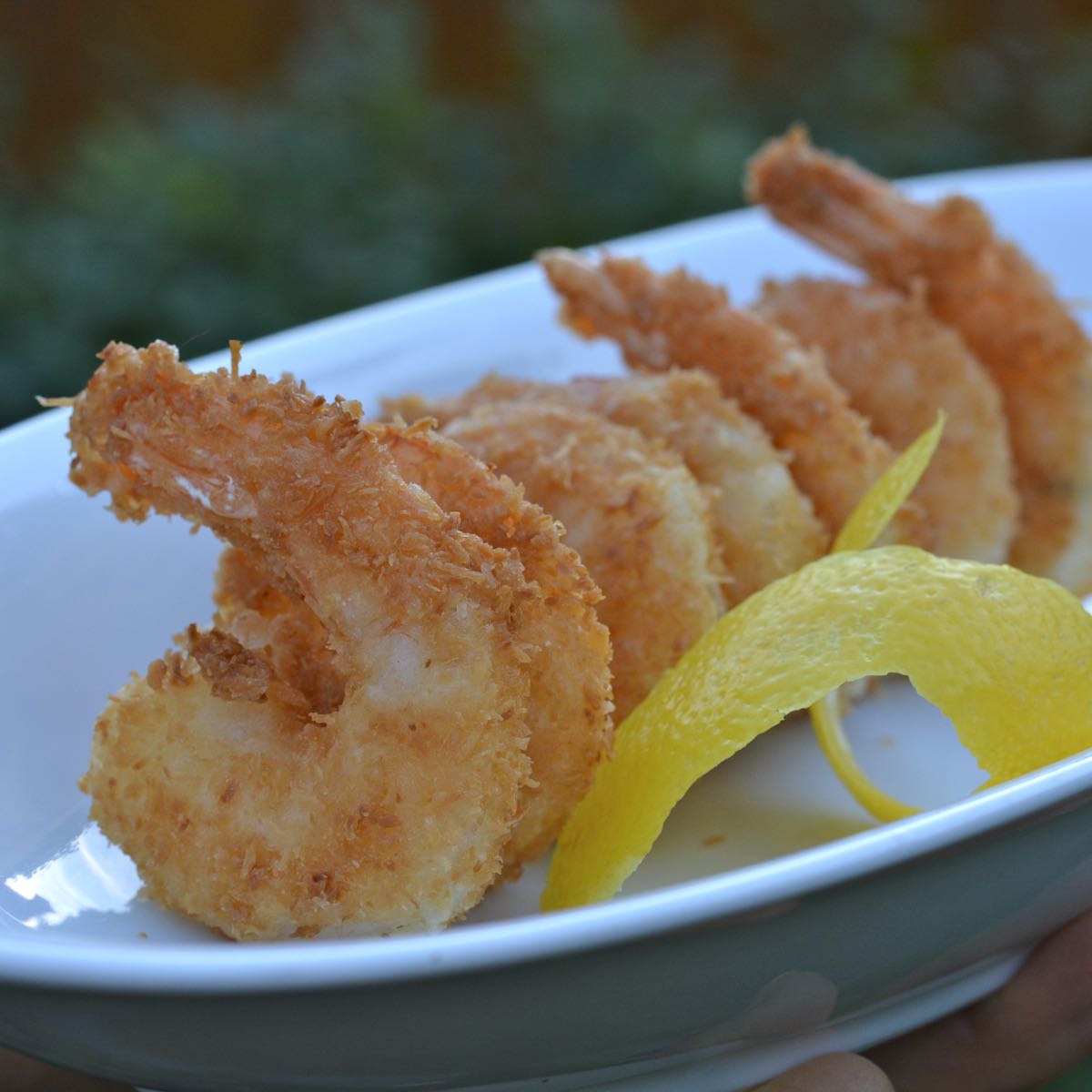 A serving dish filled with gluten free coconut shrimp garnished with a twist of lemon.