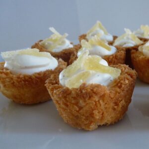 Mini coconut tartlets filled with whipping cream and topped with slivered crystallized ginger.