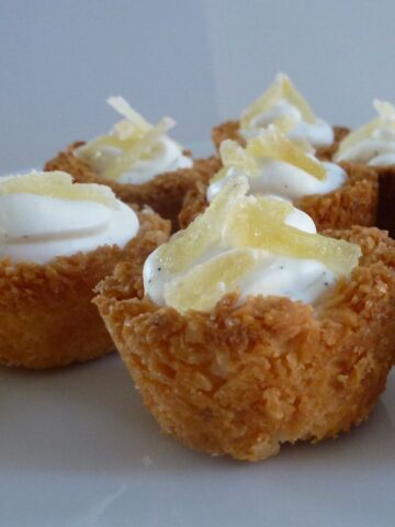 Mini coconut tartlets filled with whipping cream and topped with slivered crystallized ginger.