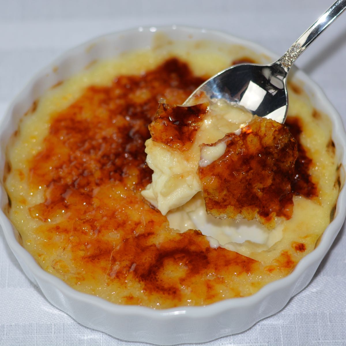 A spoonful of Creme Brulee being lifted out of a ramekin dish.
