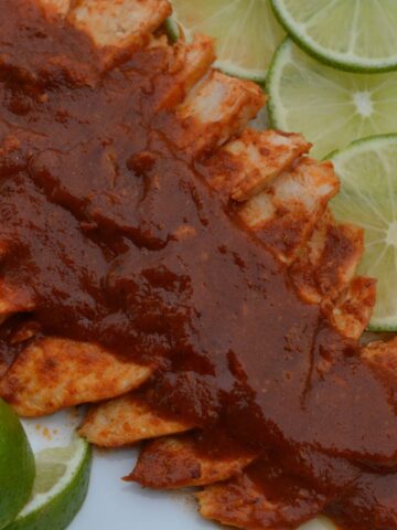A platter of Gluten Free Cumin Lime Chicken covered with sauce and garnished with fresh lime slices.