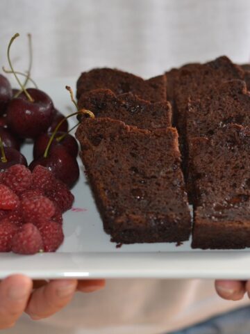 A tray of slices of Double Chocolate Banana Bread with fresh raspberries and cherries.