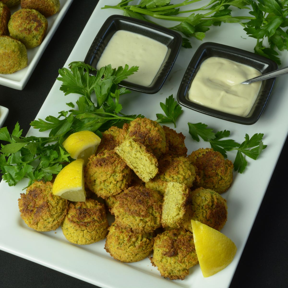 A platter of high fibre Falafel Balls with Tahini Sauce garnished with fresh parsley and lemon wedges.