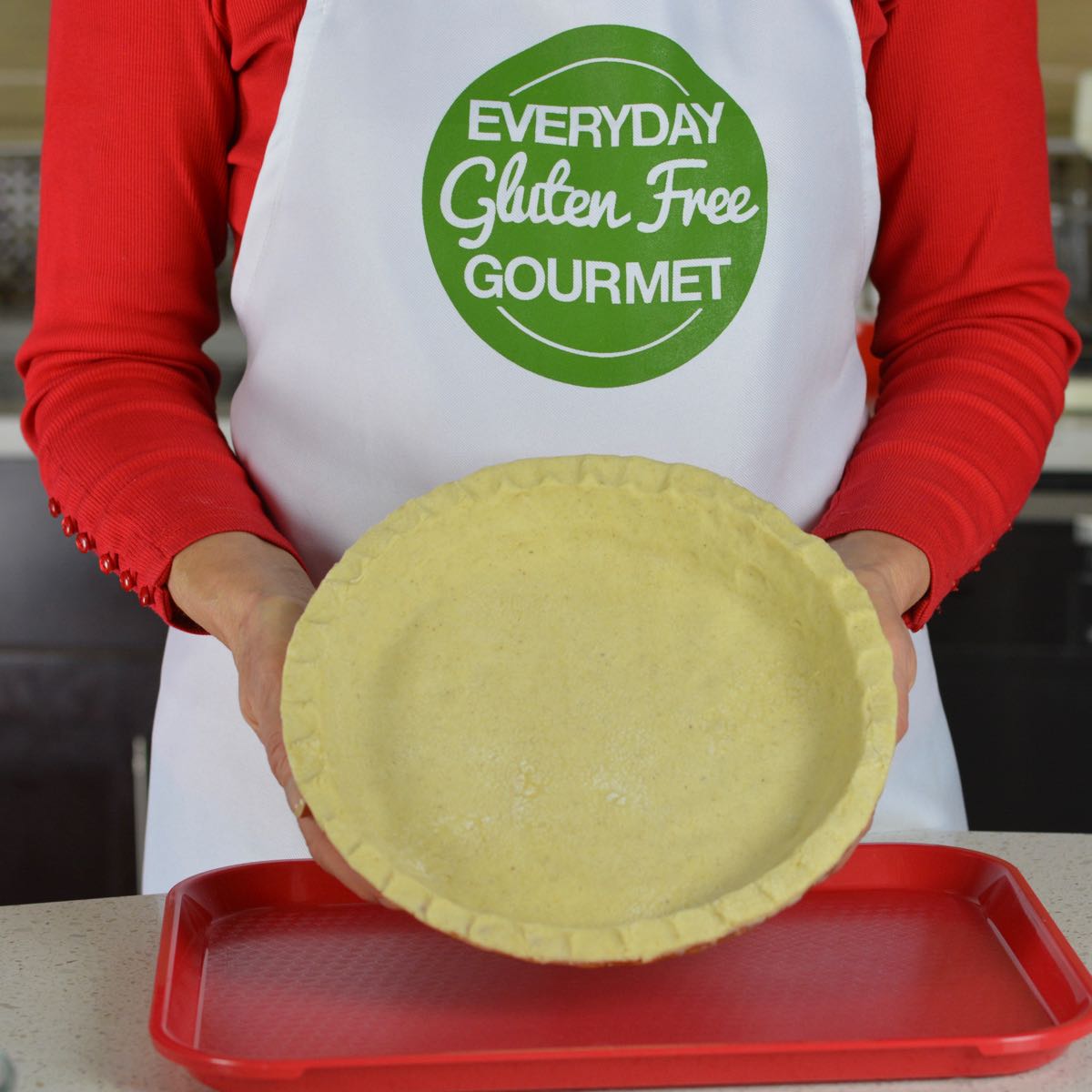 Cinde wearing her Everyday Gluten Free Gourmet apron holding a raw pie crust in a pie plate.