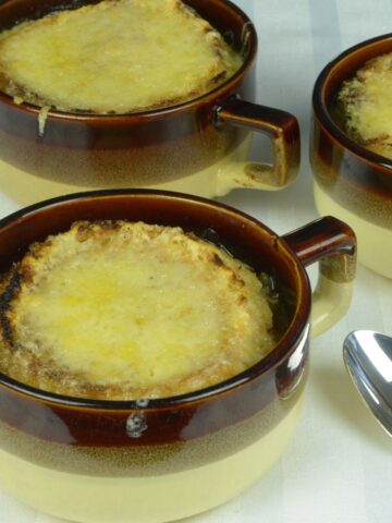 French Onion Soup in large ceramic cups with bubbly cheese melted on a gluten free crouton.