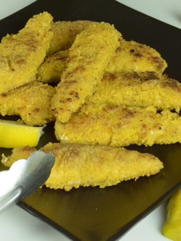 A black plate with breaded chicken strips and lemon wedges ready to serve.