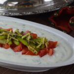 A dish of raita topped with tomatoes and peppers topped with sauteed ginger and spices.