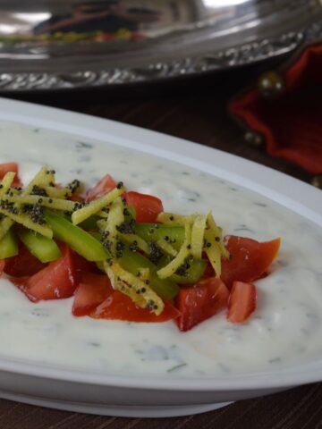 A dish of raita topped with tomatoes and peppers topped with sauteed ginger and spices.