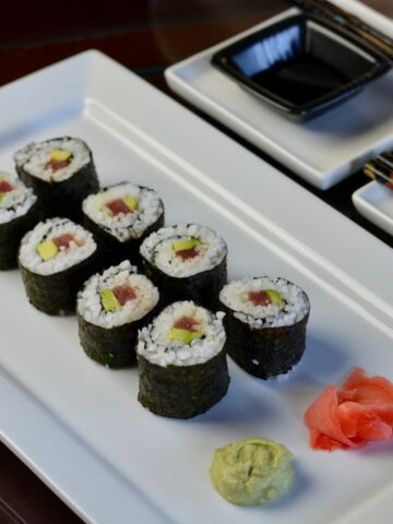 A white plate with futomaki, homemade sushi rolls, with pickled ginger and wasabi.