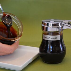 A syrup jar filled with gluten free kecap manis and another jar with a spoon of thick kecap manis slowly falling off the spoon.