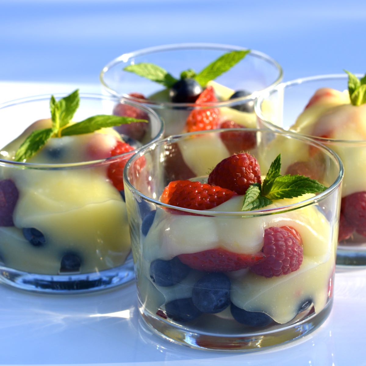 Four dishes of Lemon Curd with fresh strawberries and blueberries.