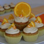 Gluten free Orange Cupcakes with orange icing on a pedestal tray, each topped with a small piece or orange.