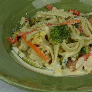 A plate of gluten free Pasta Primavera sprinkled with freshly grated Parmesan cheese.