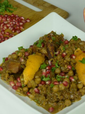 A white plate of Persian Chicken Stew sprinkled with pomegranate arils and fresh parsley.
