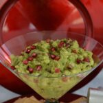 An oversized martini glass filled with Pomegranate Pear Guacamole topped with sparkling red pomegranate seeds.
