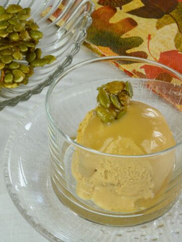 A dish of Homemade Pumpkin Ice Cream with Bourbon Caramel Sauce topped with sweet and salty candied pumpkin seeds.