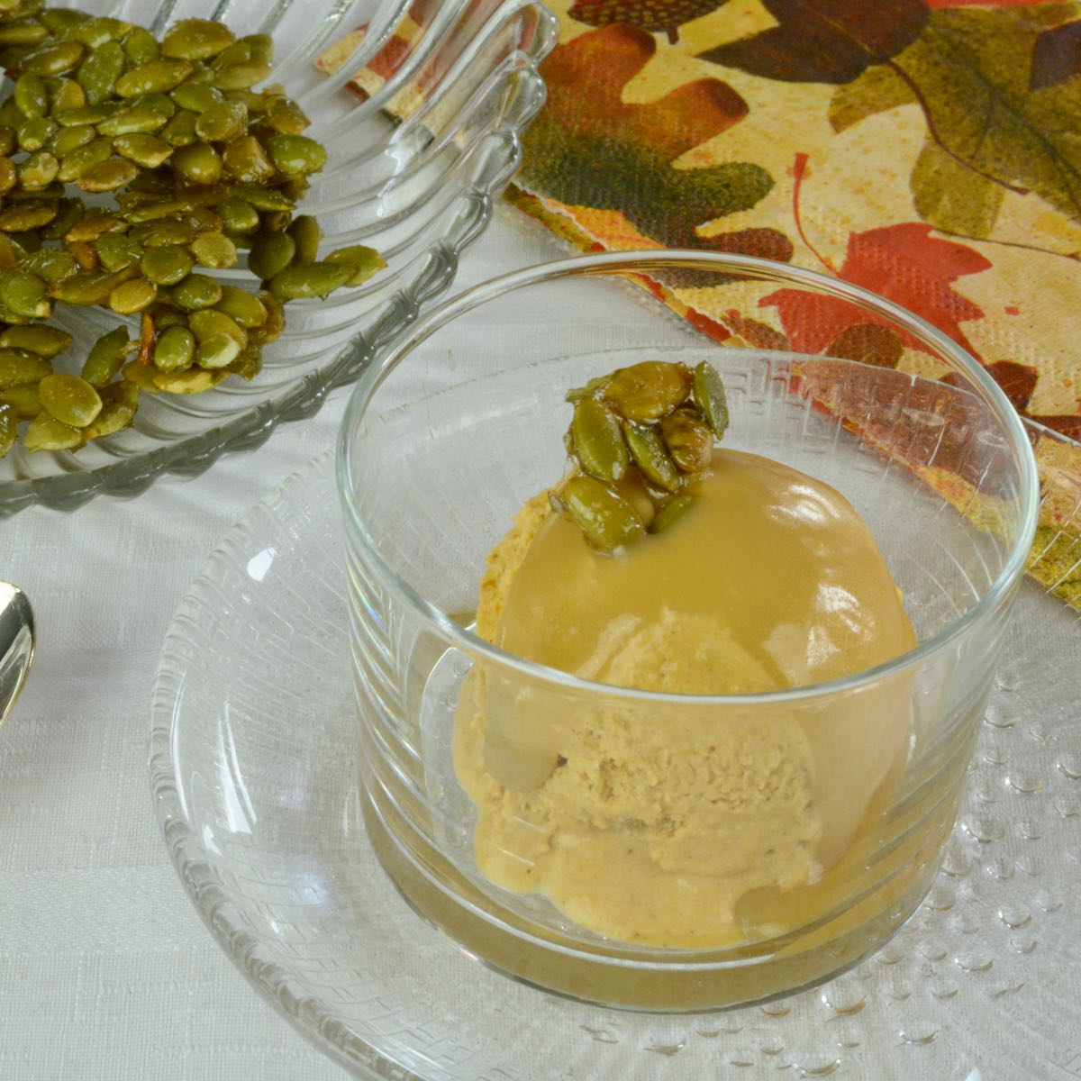 A dish of Homemade Pumpkin Ice Cream with Bourbon Caramel Sauce topped with sweet and salty candied pumpkin seeds.